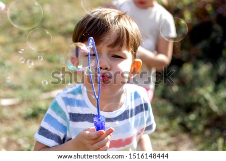 Cute little boy blowing bubbles with his sister on the backyard. Kids having fun in the nature. Bonding time. Brother and sister getting amazing time together while blowing soap bubbles. Copy-space.