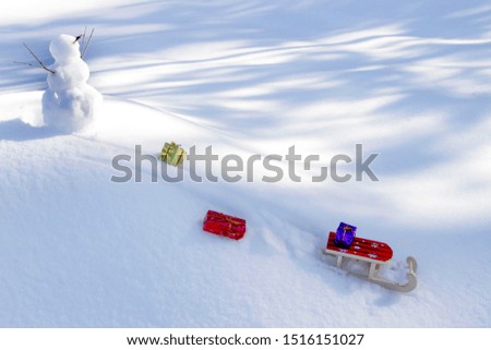 Snowman on top of a snowy mountain.  Toy wooden sled down the hill on the slope, losing gifts. Christmas card. Soft focus.