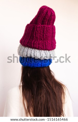 Brunette woman winter, spring or autumn portrait. Girl wearing warm clothes having fun and comfort. Model in casual beige sweater and pink, blue, grey hat. Woman wear 3 hat. Look from back.