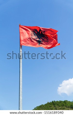 Albania flag against blue sky with white clouds. The Albanian flag is a red flag with a silhouetted black two-headed eagle.Vertical image.