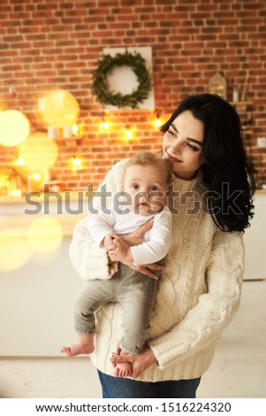 A beautiful young mother with a baby in a Christmas decorated room near the Christmas tree on a background of lights and music