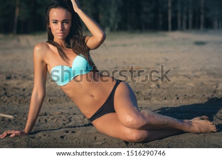 young woman in a turquoise swimsuit near the water sunbathing on the beach.