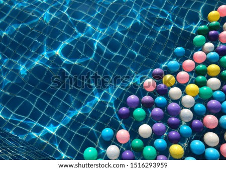 Multicolored plastic ball floating on the surface of swimming pool with transparent water, beautiful distorted tiled floor under water and pattern of line, light and shadow from water ripple.