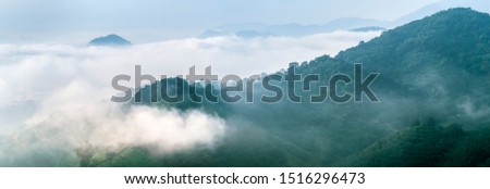 The slope of the mountain in a forest covered with little clouds and green trees in a beautiful landscape.Photos of dark mountain scenery with gray clouds and rain Panorama and soft focus picture