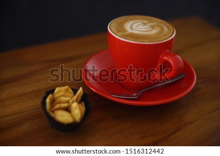 Cappucino coffe in a red cup on a wooden table.