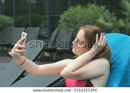 Beautiful girl takes a selfie on a smartphone, sits by the pool in a bathing suit