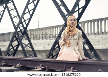 Beautiful female model wearing peplum dress with hijab, posing on abandoned railroads bridge. Stylish Muslim hijab fashion lifestyle portraiture concept.