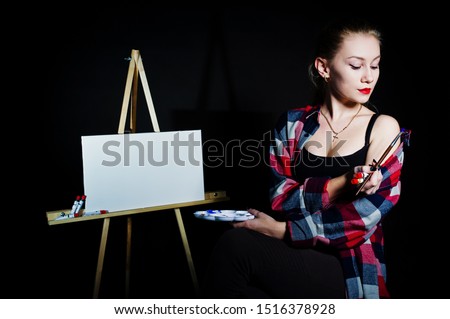Beautiful woman artist painter with brushes and oil canvas posing in studio isolated on black.