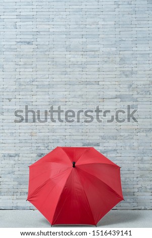 The red umbrella stands out from the white brick wall.