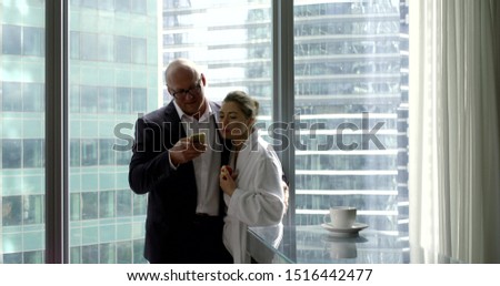 A man entrepreneur in a business suit in the morning in his apartment with large Windows hugs his beloved wife and writes a text message on his mobile phone