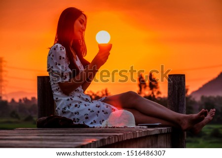 Beautiful sunset with woman sitting and sipping coffee at sunrise while the sun is falling into coffee mug with orange sky color and farmland background
