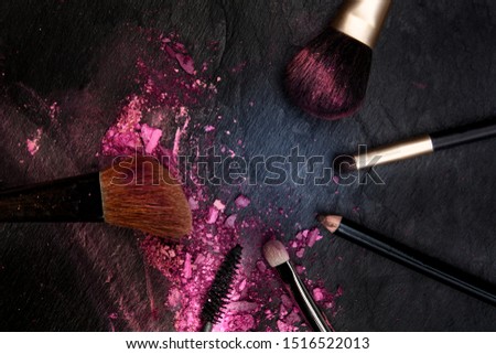 Make-up brushes with crushed cosmetics, shot from above on a black background forming a frame for copy space, a beauty design template for a makeup banner