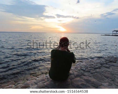 50-year-old man in denim shorts and T-shirt photographing the Rio Negro on Ponta Negra beach in Manaus, the Amazon region, in the late afternoon