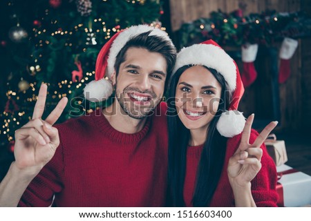 Close up photo of two married romance romantic people with cap hat make v-signs enjoy christmas vacation x-mas holidays in house full of noel decoration illumination newyear lights indoors