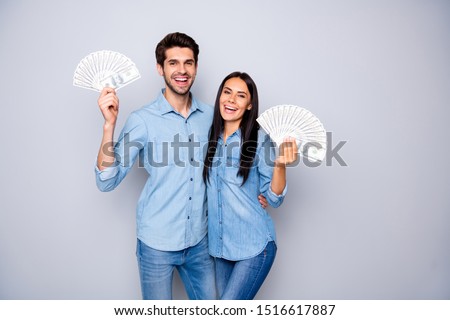 Photo of two people hugging while holding money they won wearing jeans denim shirt smiling toothily having fun isolated over grey color background