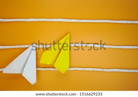 Yellow and white paper plane on orange background with white rope laid horizontally as level to overcome, improvement and effort to achieve goal or mission concept 