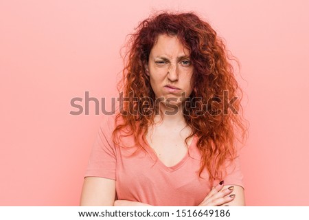 Young natural and authentic redhead woman unhappy looking in camera with sarcastic expression.