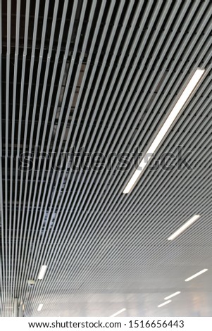 View of a modern ceiling with lights in a large public space. Abstract picture with parallel grey and white lines. Striped textured surface. Geometric shapes in background.