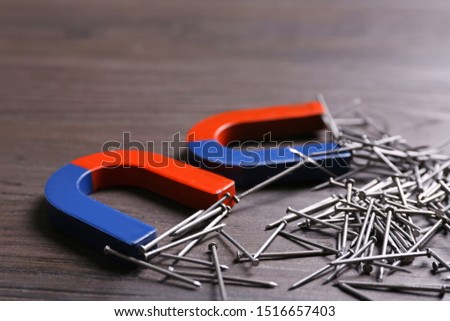 Magnets attracting nails on dark grey wooden background, closeup