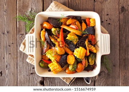Roasted autumn vegetables in a baking dish, top view over a rustic wood background