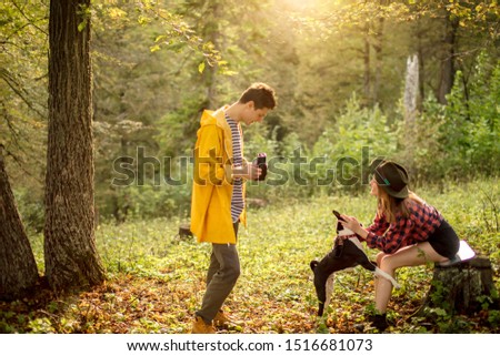 young tourists testing old camera, girl is playing with a pet in the forest. side view photo. spare time, hobby, interest