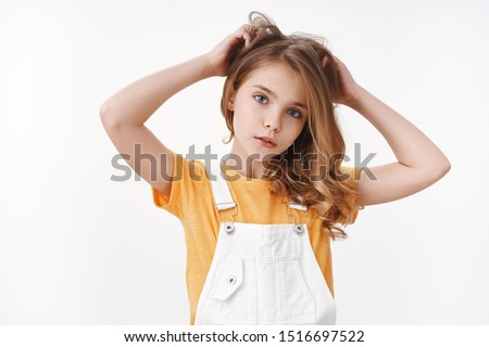 Tender lovely young blond girl in summer dungarees over yellow t-shirt, look thoughtful and cute camera, scratch hair bothered, touch hairstyle, suffer head lice, lacking vitamins, white background
