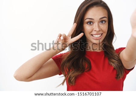 Close-up upbeat tender feminine young brunette woman, hold smartphone one hand, showing goodwill and wellbeing sign, victory or peace gesture, smiling silly, express enthusiasm, white background