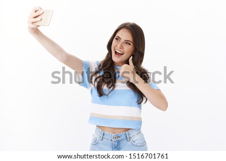 Optimistic lucky cute female feeling happy, travel around world taking selfies, extend arm with smartphone joyfully smiling, pose near beautiful sightseeing show thumb up approval gesture