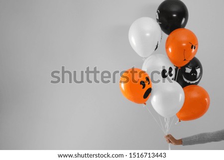 Woman holding color balloons for Halloween party on light grey background, closeup. Space for text