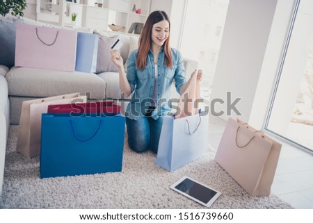 Full size photo of cheerful positive redhair girl sit on floor carpet hod plastic card check her packages purchase wear denim jeans clothes indoors