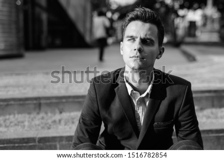 Young handsome businessman sitting outdoors shot in black and white