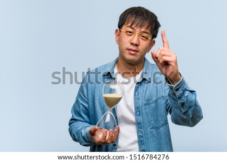 Young chinese man holding a sand timer showing number one