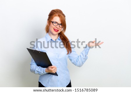 Young beautiful redhead businesswoman wearing eyeglasses holding flip board on grya background