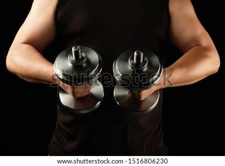 man in black clothes holds steel dumbbells in his hands, his muscles are tense, low key, sports background
