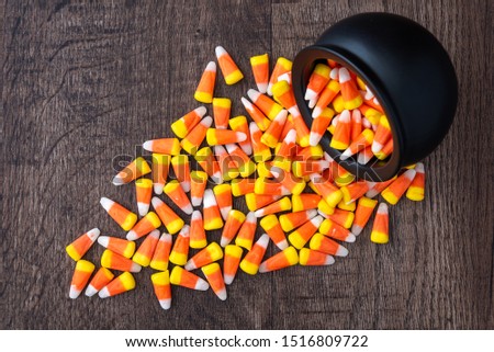 Black ceramic cauldron filled with holiday candy corn tipped over on a rustic wood background, spilling over onto the background
