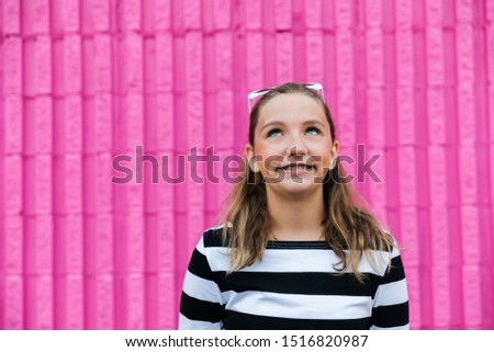 Cute caucasian girl with braces in front of a hot pink wall outside laughing and looking up