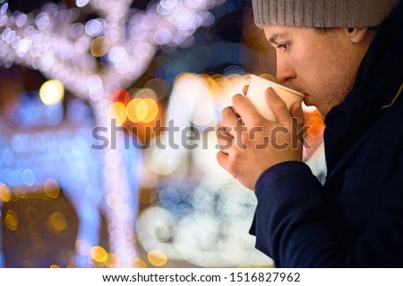 The guy holds holds hot tea in his hands on a background of Christmas lights. hot drinks, holidays and people concept - close up