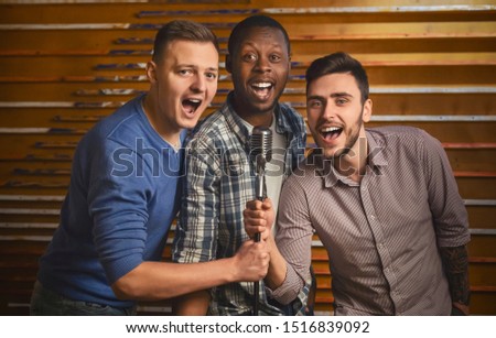 Happy multiracial men singing at karaoke bar, spending time together on friday night