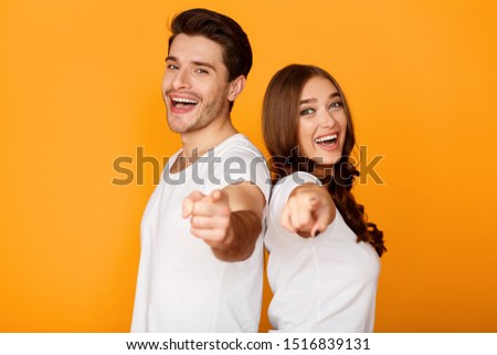 Gotcha! Cheerful man and woman pointing fingers at camera, yellow studio background