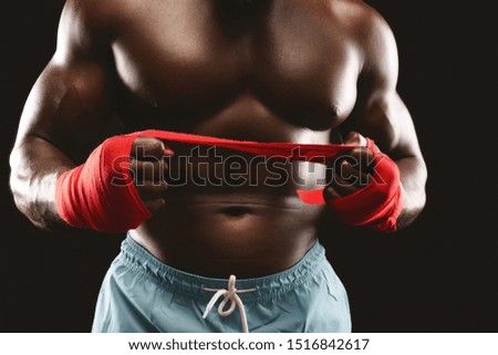 Strength and power concept. Professional black fighter pulling red boxing bandage, black studio background, cropped