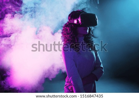 Virtual reality game. A girl in a VR helmet plays a game or explores the environment. Portrait in neon light, futuristic image in smoke