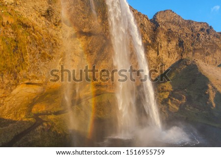 Waterfall Seljalandsfoss (part of Seljalands river taking its origin in Eyjafjallajökull volcano glacier), as pictured with rainbow caused by thick spray during the in sunset hour 