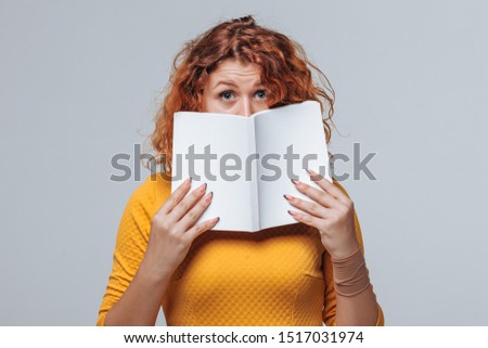 The red-haired girl covered her face with a white book