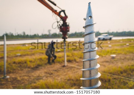 technician installing ground screw for mounting structure of solar panel at solar farm