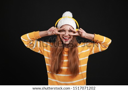 Young woman listening to music with headphones on black background