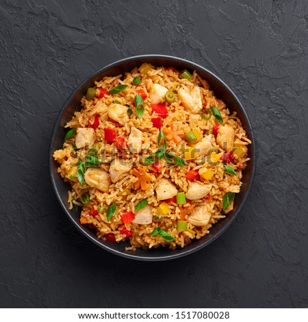 Schezwan Chicken Fried Rice in black bowl at dark slate background. Szechuan Rice is indo-chinese cuisine dish with bell peppers, green beans, carrot, chicken breasts. Copy space. Top view Royalty-Free Stock Photo #1517080028