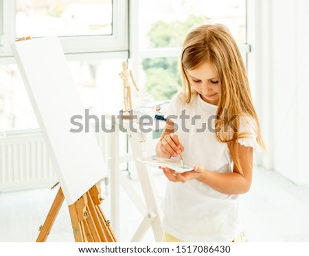 Cute little girl paints on canvas in a spacious white room