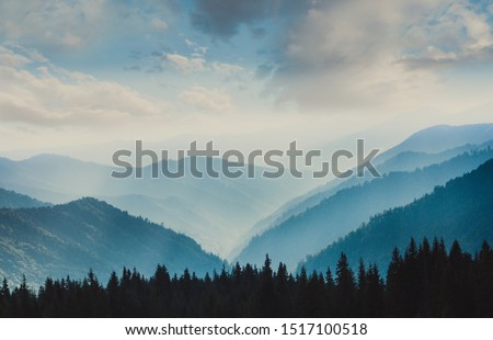 Landscape of misty mountains. View of coniferous forest, layers of mountain and haze in the hills at distance. Beautiful cloudy sky. Tourism and travelling. Royalty-Free Stock Photo #1517100518