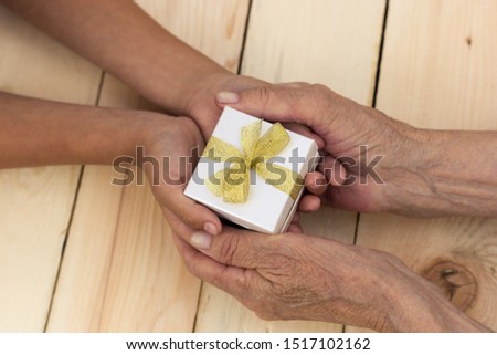 Hands of an elderly man and children's hands are holding a box with a gift. The concept of caring for old people, giving a gift for the holidays, birthday, Christmas. Image. Royalty-Free Stock Photo #1517102162