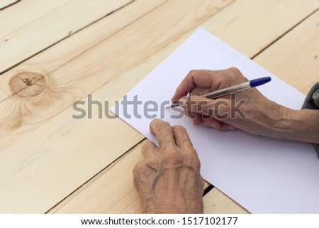 Hands of an elderly man are holding blank paper and a pen. Concept of testament, signing of an agreement, writing in old age. Image. Royalty-Free Stock Photo #1517102177